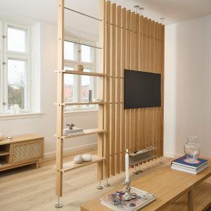 WoodUpp Raumteiler aus hellen Eichenlamellen mit integrierter TV‑Halterung, schmalem Ablageboard und sichtbaren Edelstahlfüßen. Dazu freistehendes WoodUpp Regal mit offenen Böden und dekorativen Objekten. Ergänzt durch WoodUpp Sideboard und niedrigen Holztisch in gleichem natürlichem Eichenfinish für luftige, skandinavische Raumtrennung und Stauraum.